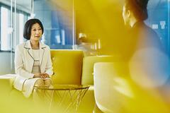 Women in an office talking. Japan. Primary color: yellow.